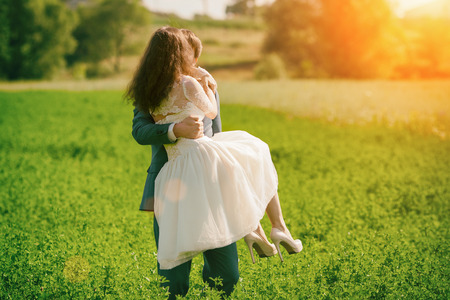 Happy kissing wedding couple outdoors on the meadow. Man is holding woman in his armsの写真素材