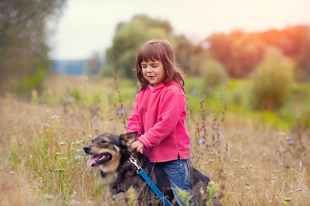 Happy little girl walking with dog on the meadowの写真素材