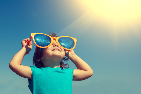 Happy little girl with big sunglasses looking at the sunの販売画像