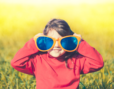 Happy little girl wearing big sunglasses in the meadowの写真素材