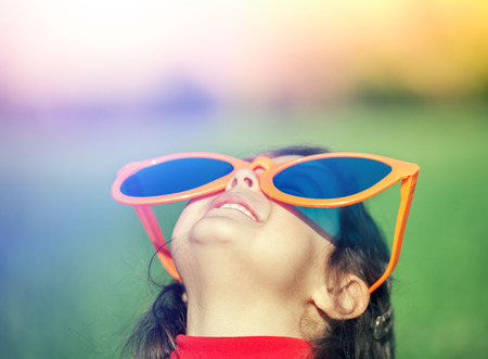 Happy little girl with big sunglasses walking in the meadow and looking at the sunの写真素材