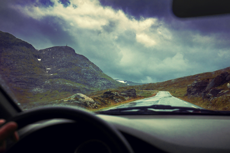 Driving a car on mountain road. Road among mountains with dramatic stormy cloudy sky.  Beautiful nature Norway. Sunsetの写真素材