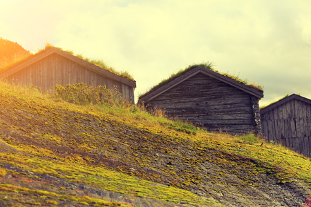 Wooden fishermen's houses with green grass on roofs against cloudy sky on mountainの写真素材
