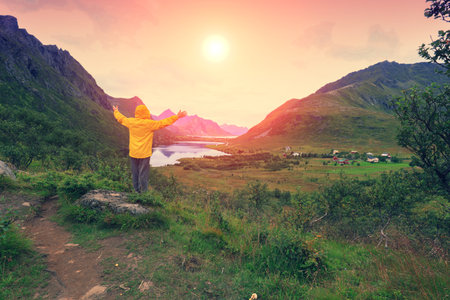 Panoramic view of the fjord. Twilight time with an amazing orange sky. The young man with hands in...