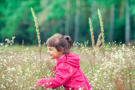 Happy little girl walking on the flower meadow in sunny dayの写真素材