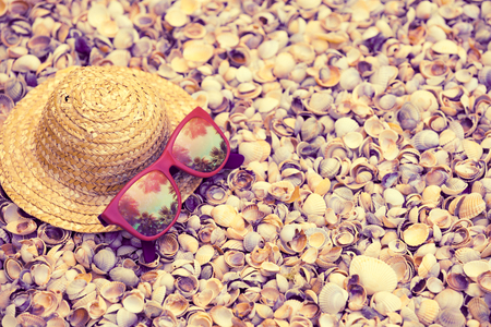 Beach scene. Straw sun hat and sunglasses with reflection of palm trees lie on sea coquina shellsの写真素材