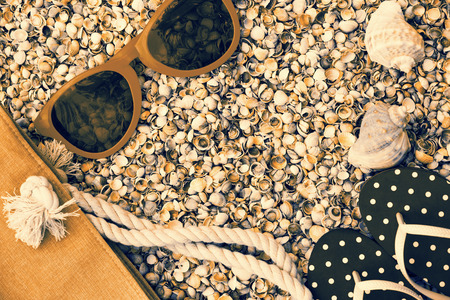 Beach scene. Woman accessories. Sunglasses, flip flop sandals and beach bag lying on sea coquina shellsの写真素材