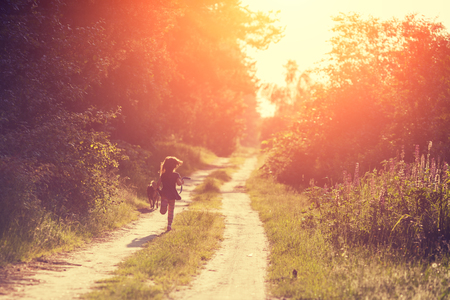 A little girl with a dog runs along a country roadの写真素材