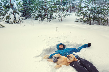Best friends. Happy man with Labrador retriever dog lying in snowy winter forest. Man enjoying snow