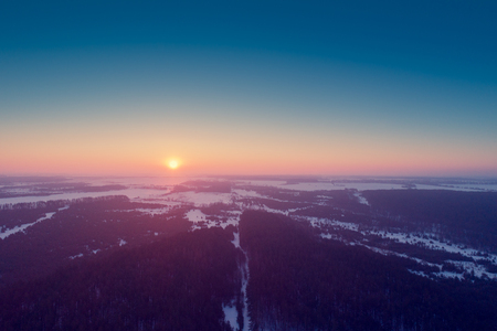 Aerial evening view at countryside and snowy fields and forest during sunsetの写真素材