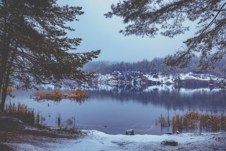 Beautiful rocky lake with pine trees. Lake in the winter in snowfallの写真素材
