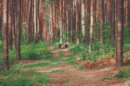 Young man sitting with a dog in the summer pine forest