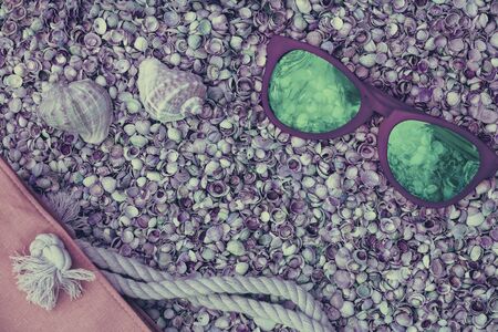 Beach scene. Sunglasses and beach bag lying on sea coquina shellsの写真素材