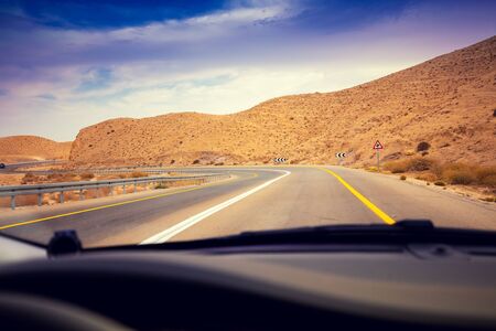 Driving a car on the mountain road in the desert. View of sandstone mountains through the windscreen. The road from Arad to the Dead Sea. Israelの写真素材