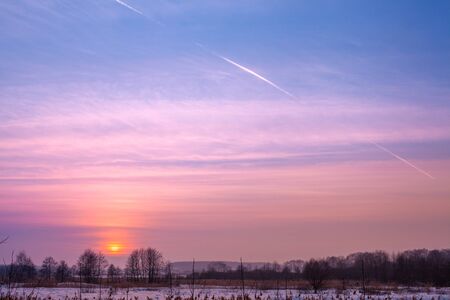Winter landscape. Evening in the countryside. Sunset with beautiful gradient sky in the field covered with snow. Rural landscape with magical light.の写真素材