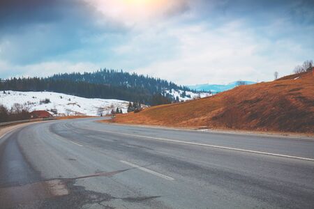 Empty winter winding mountain road with dramatic cloudy skyの写真素材