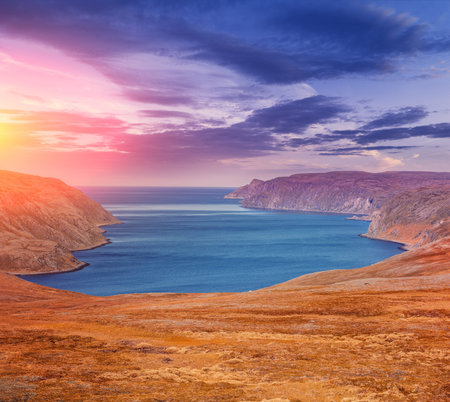 Barents sea, fjord in the evening. Beautiful rocky seashore with dramatic sunset sky. Shoreline in...
