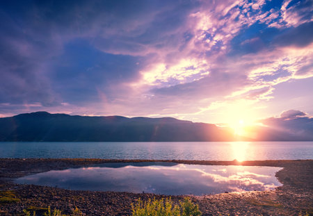 Fjord in the light of sunset. Mountain range on the horizon. Rocks in the sea at sunset. Seascape in...