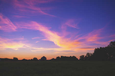 Rural landscape with beautiful gradient evening sky at sunset. Green field and village on horizonの写真素材