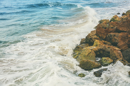 Sea surf on a rocky shore with large brown stonesの写真素材