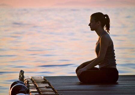 Youn Woman meditating at sunrise, sea at backgroundの写真素材