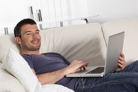 beautiful young man on sofa with computerの写真素材