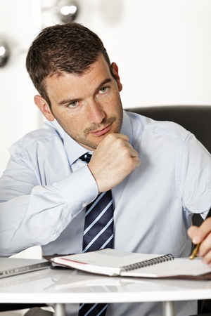 young pensive businessman in office with penの写真素材