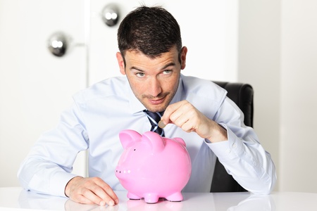 young man with pink piggy bank and coinの写真素材