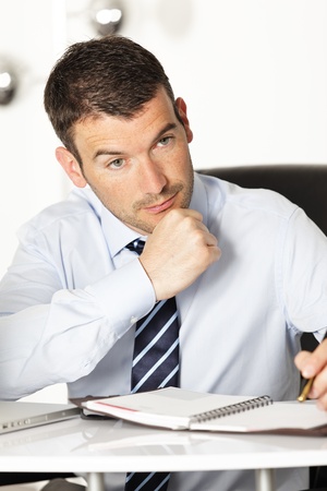 pensive young businessman with pen in officeの写真素材