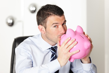 young man in office kissing a pink piggy bankの写真素材