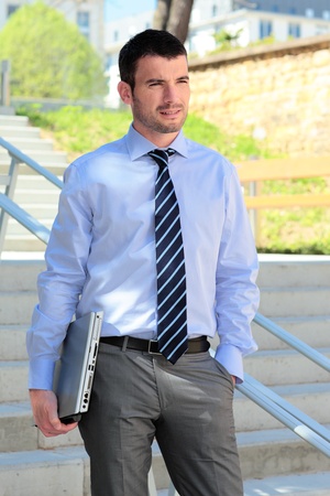 standing businessman waiting outdoor with laptop on stairsの写真素材