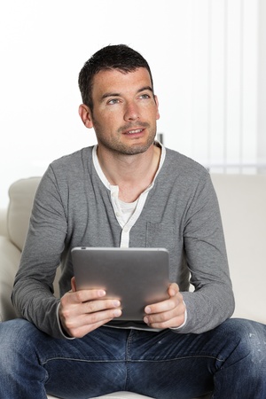 handsome man on sofa with tablet looking someoneの写真素材