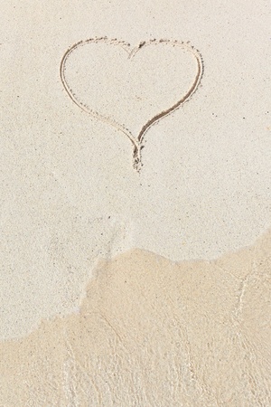 handwritten heart on sand with wave approaching on a beachの写真素材