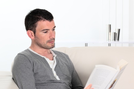 man reading a novel book while relaxing on sofa の写真素材