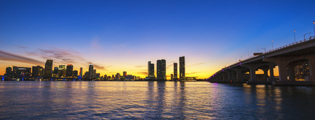 Miami city skyline panorama at dusk with urban skyscrapers and bridge over sea with reflection の写真素材
