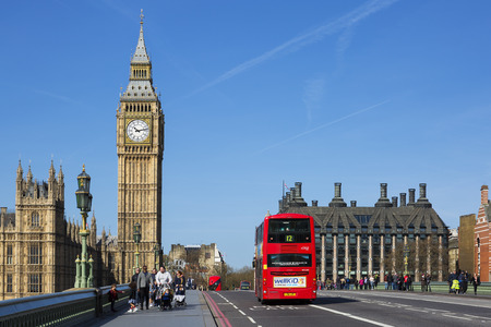 LONDON, UK - APRIL 12, 2015: double-decker bus passes pedestrians walking in front of Big Ben and Houses of Parliament on Westminster Bridge.のeditorial素材