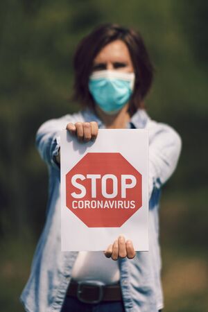 Beautiful woman with mask holding a sign "stop coronavirus"の写真素材