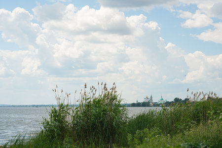 Green trees by the lake on a sunny day, with clouds on the sky. Orthodox monastery in the background. High quality photoの写真素材