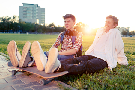 Two teenagers in a good mood with a skateboard rest in the park at sunset of the dayの写真素材