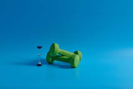 two green dumbbells and an hourglass on a blue backgroundの写真素材