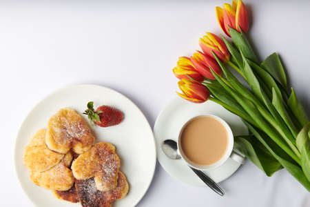 a cup of tea with a spoon and cheesecakes in the form of hearts and a strawberryの写真素材