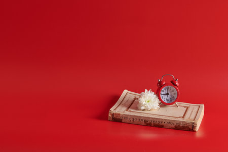 the alarm clock stands on a closed book on a red backgroundの写真素材