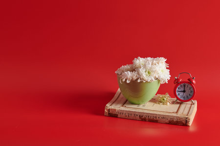 on a closed book there are white flowers in a green cup with an alarm clockの写真素材