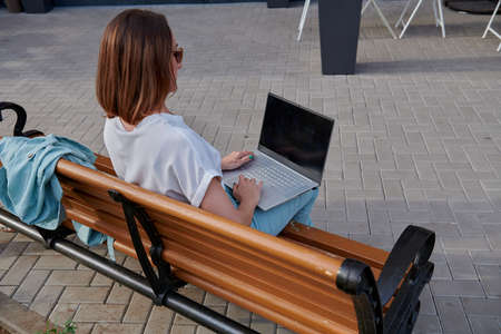 redhead woman sitting on bench and working on laptopの写真素材