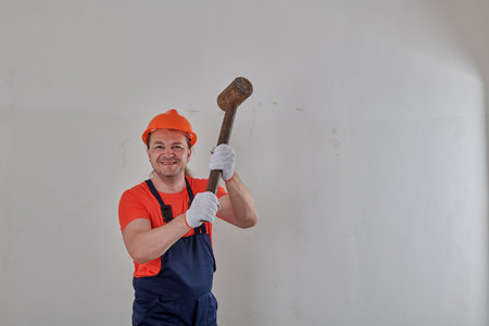 cheerful man with a sledgehammer in his hands in a helmetの写真素材