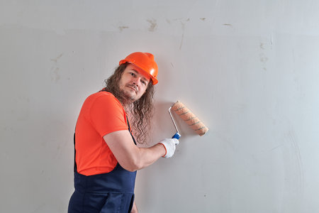 a painter in a bright T-shirt stands against the wall with a roller