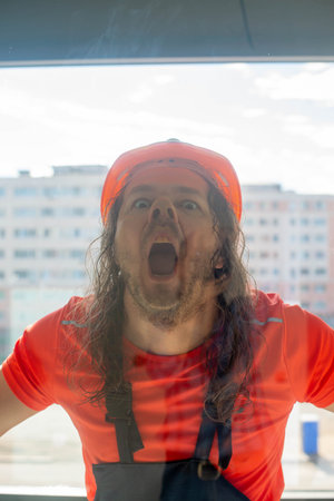 funny engineer in a helmet makes a face behind the glassの写真素材