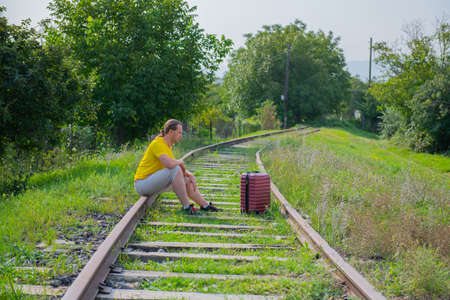 sad man with red suitcase on the railroad sitsの写真素材