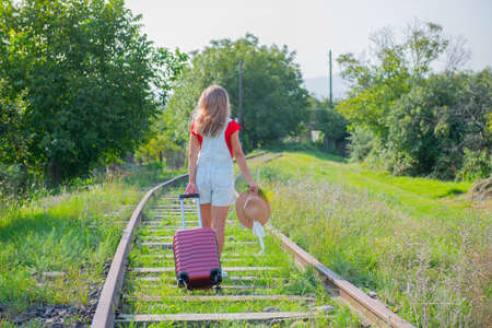 girl with a hat walking on the railroad with a suitcase. High quality photoの写真素材