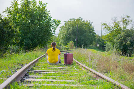 sad traveler with red suitcase on the railroad sits. High quality photoの写真素材